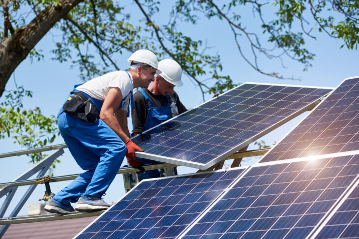 Two construction workers installing solar panels on a roof
