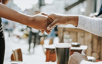 A close up shot of two people shaking hands over a coffee cup outdoors.