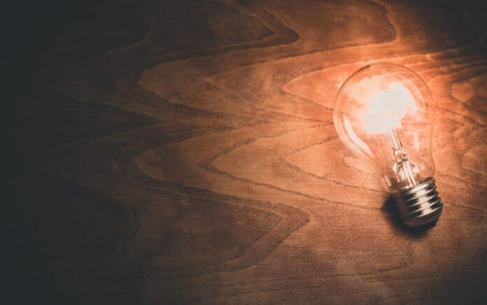 A birds-eye-view shot of a lightbulb laying down on a wooden background, the lightbulb is lit.