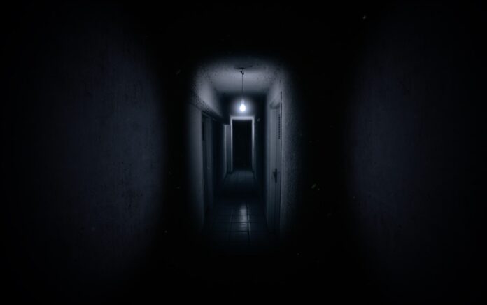 A photograph of a dark hallway, with a lightbulb only lighting the end of the hallway.
