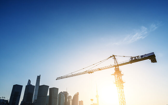A wide landscape shot of a large crane with the London skyline in the background and sunlight breaking through from the far background