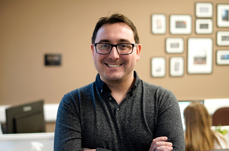 Steve Jenkinson, Creative Strategist & Copywriter, standing in an office with a colleague sat at a desk in the background