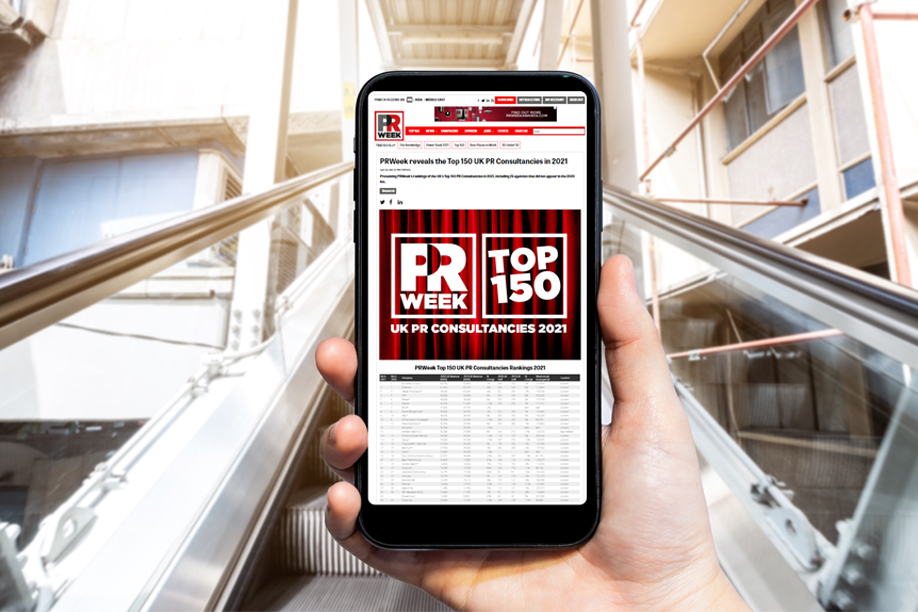 A close up shot of a mobile phone being held up in front of an escalator, with a news article on screen