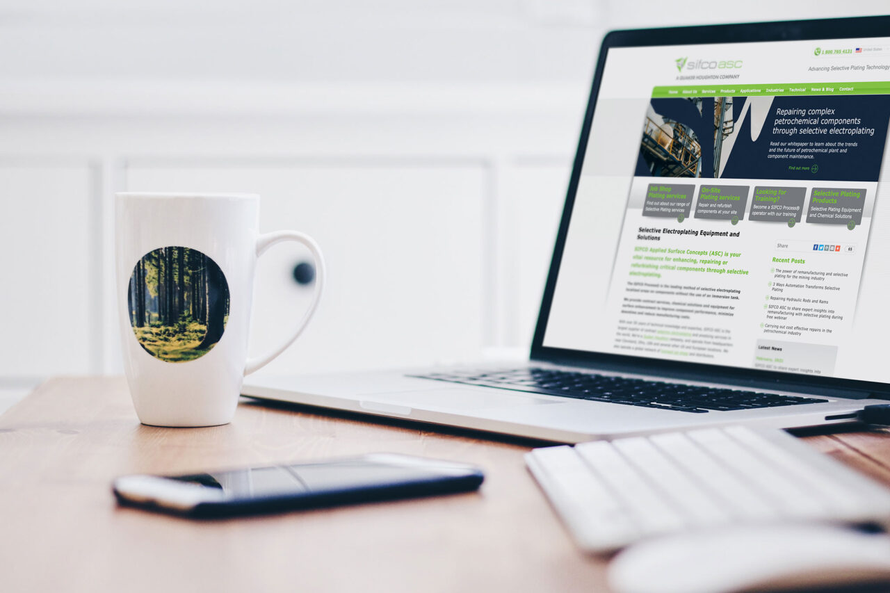 A laptop showing a website about electroplating, a coffee cup and a mobile phone rests next to the laptop