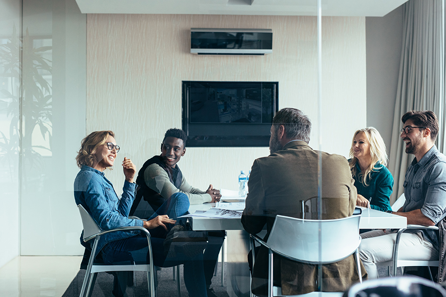 A wide shot of an office meeting room with a table full of smiling workers, taken through the window