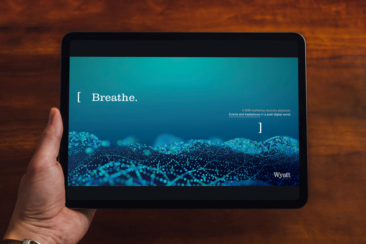 a close up shot of a hand holding an electronic tablet, with wyatt branding on screen, against a wooden background