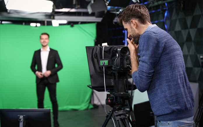 A shot of a filming shoot, with a man recording a video in front of a green screen.
