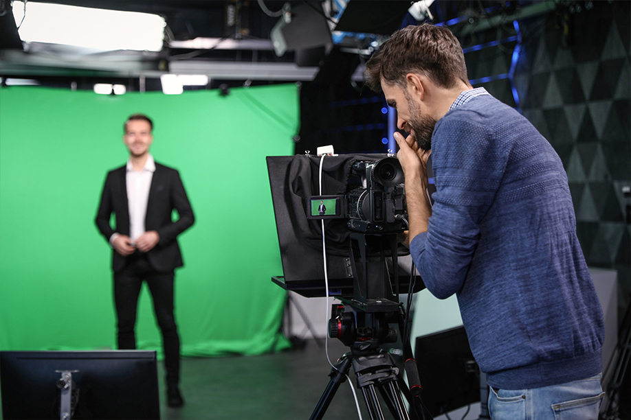 A shot of a filming shoot, with a man recording a video in front of a green screen.