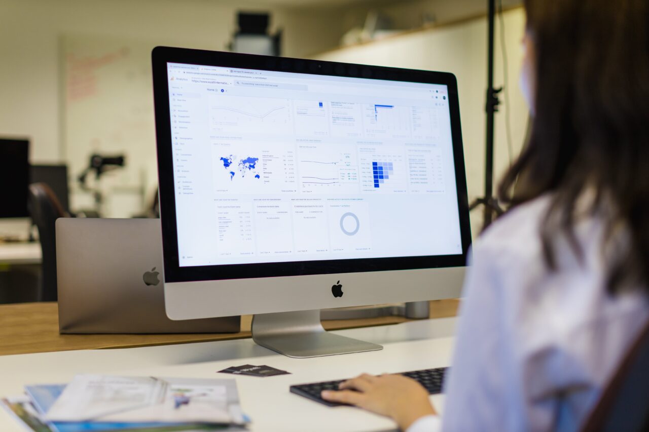 An over the shoulder shot of a female office worker looking at a computer screen, with various graphs on screen.