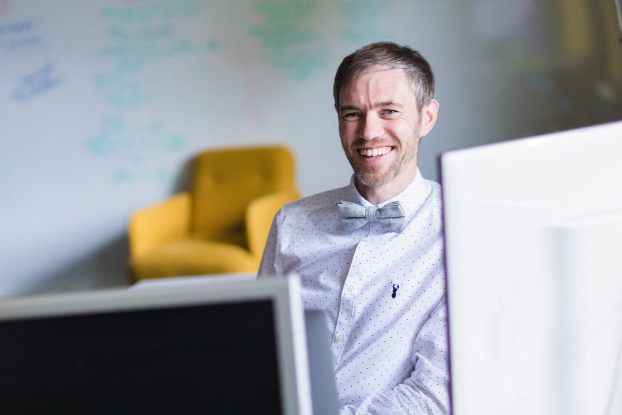 Simon Hall, Brand and Strategy Director, sitting behind two computer screens and smiling
