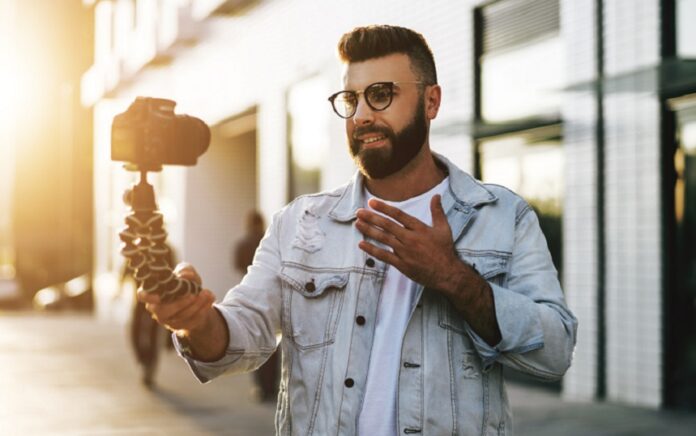 Male vlogger making video content outdoors with pedestrians in the background