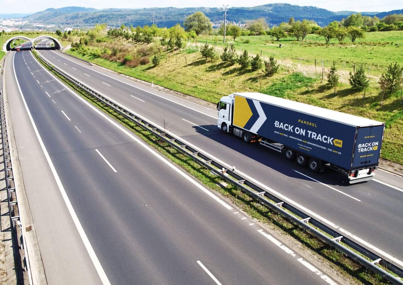 A wide shot of a Pandrol lorry that is driving along an empty motorway with greenery either side and mountains in the distance