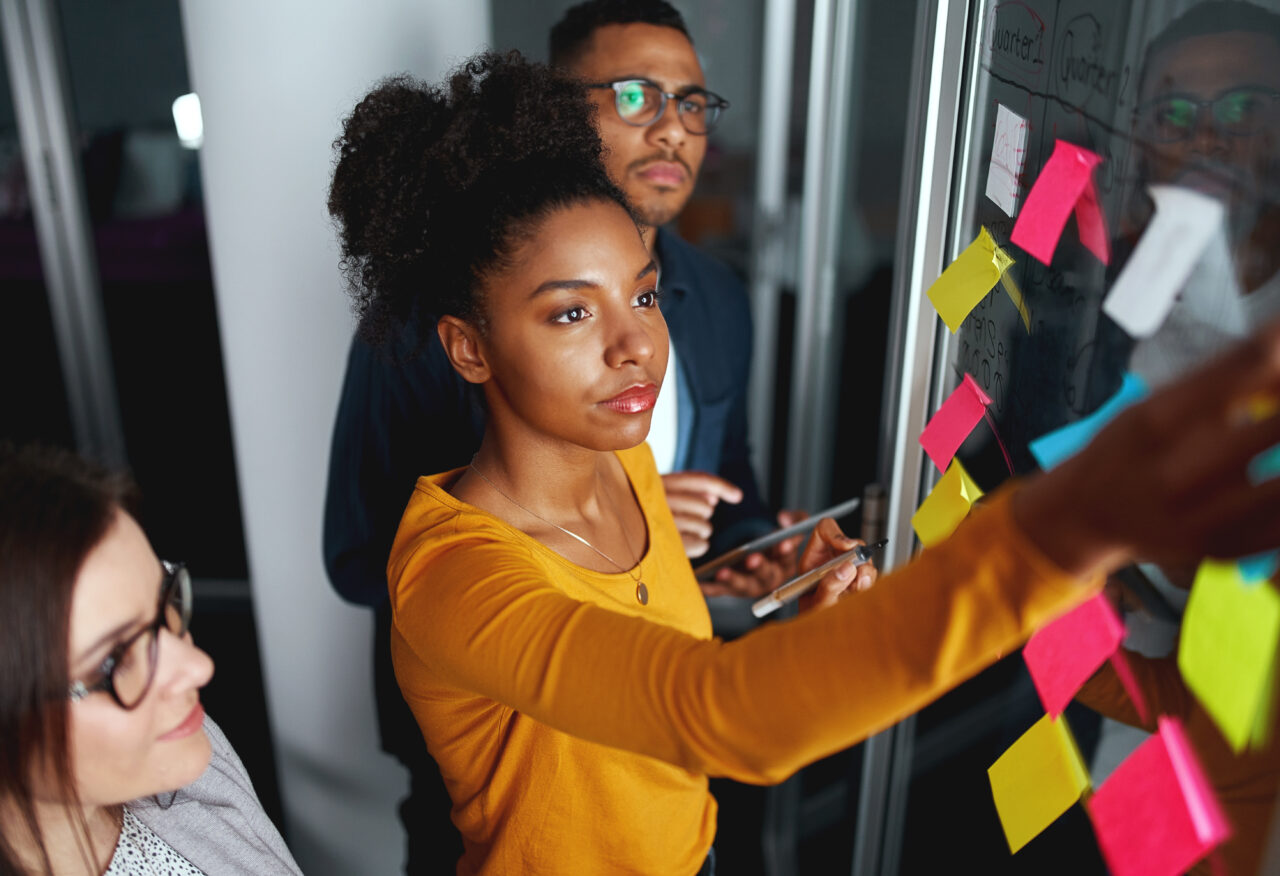 Two females and one male are all looking at a number of sticky notes attached to a window