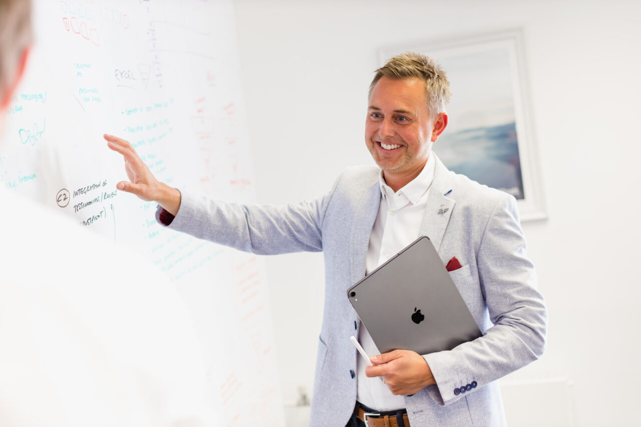 Mark Fones, Managing Director, standing smiling in front of a whiteboard holding an electronic tablet