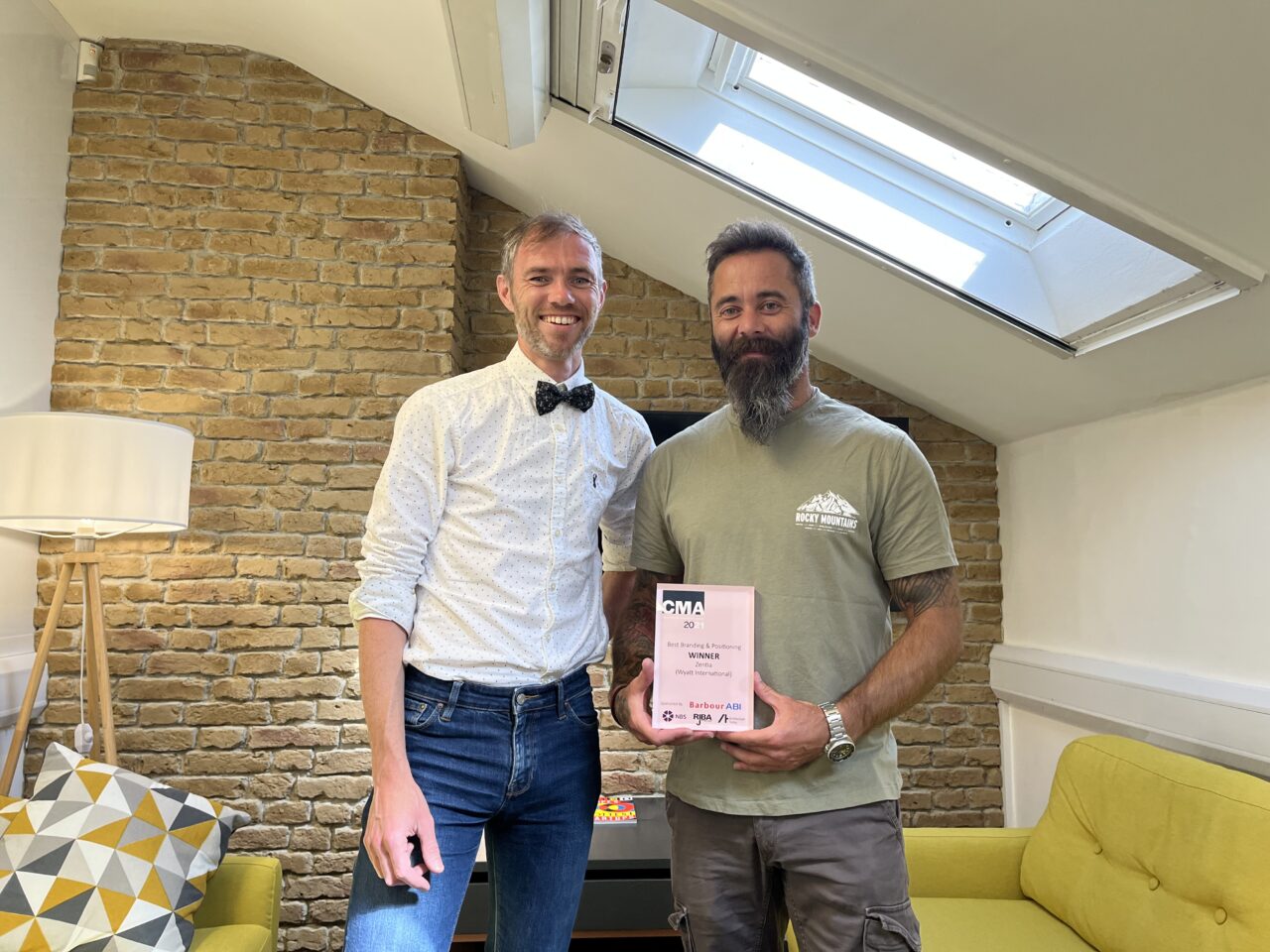 Simon Hall, Brand and Strategy Director, and Mark Fletcher, Senior Designer both standing and smiling in an office holding a CMA award