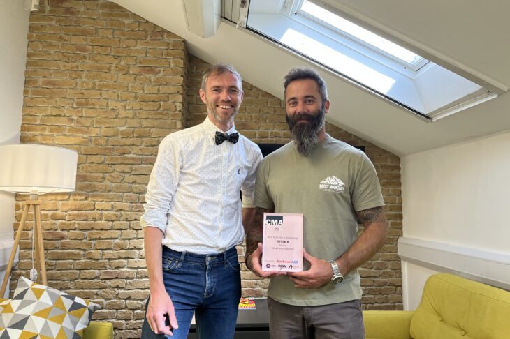 Simon Hall, Brand and Strategy Director, and Mark Fletcher, Senior Designer both standing and smiling in an office holding a CMA award