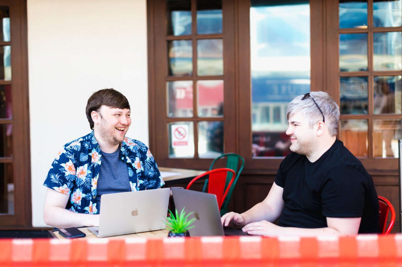 Lee Savery, Digital Content and SEO Manager, and Ben Baker-Holyhead, Strategic Account Director, having a conversation and working on tables outside.