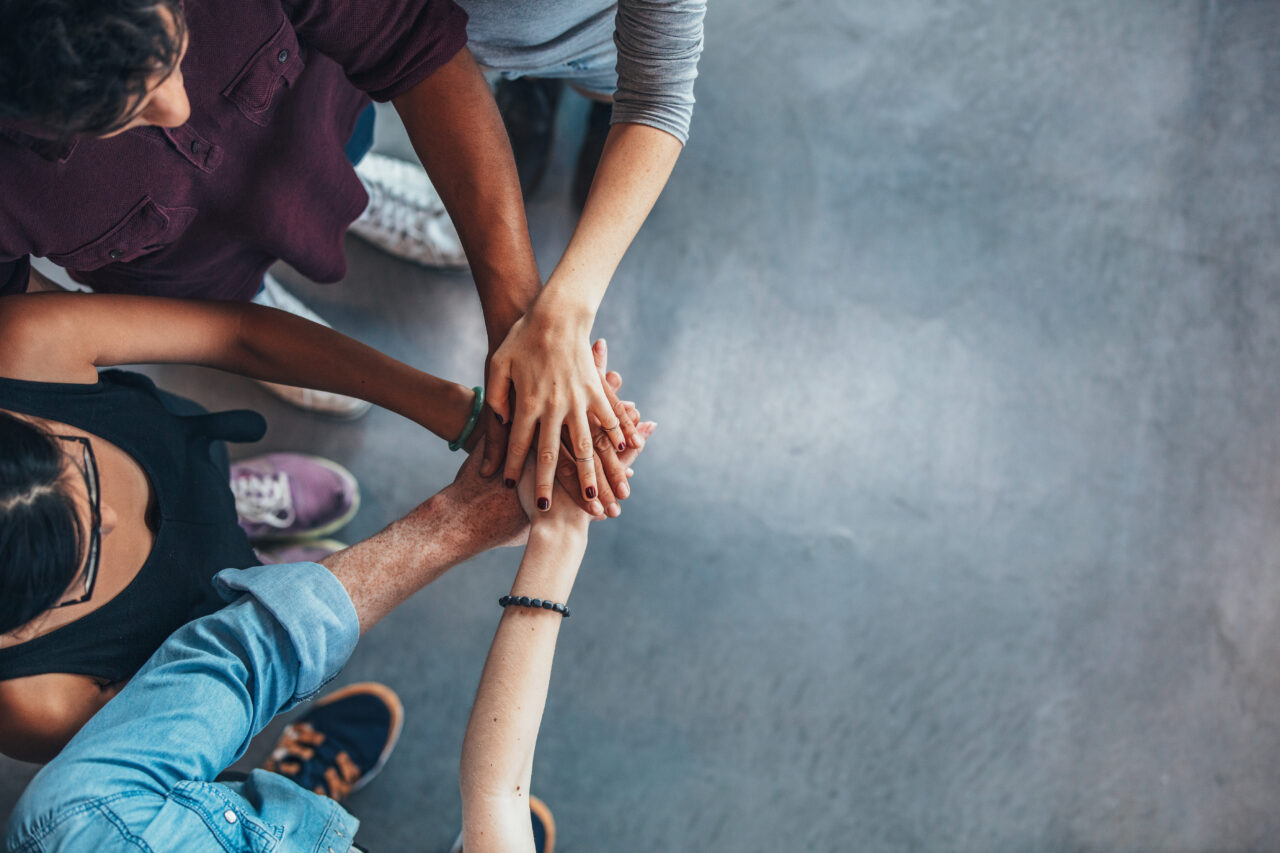 Top view image of group of young people putting their hands together.