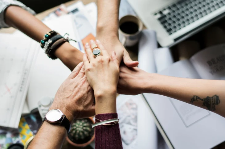 Team putting hands together with laptops and work in background