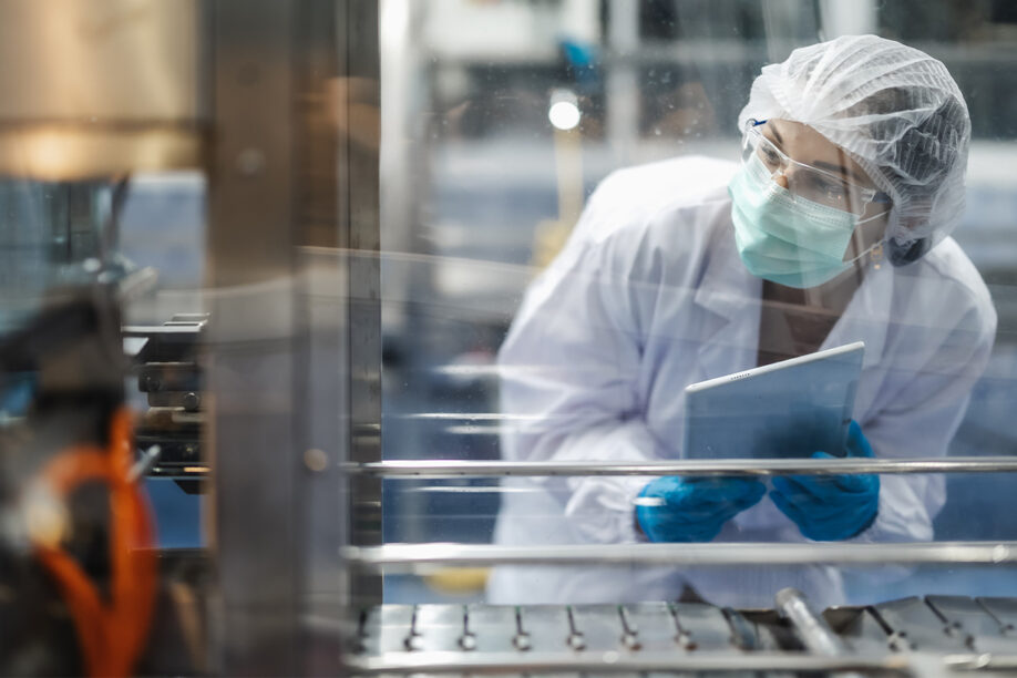 A woman wearing a lab coat and gloves is using a tablet, engaged in her work in a scientific environment.