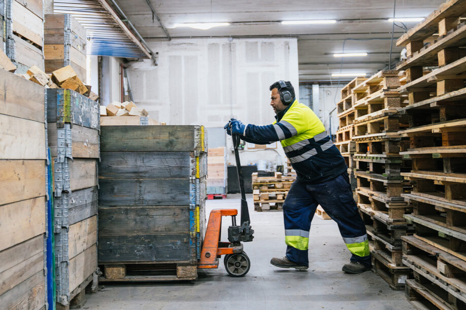 A worker transports pallets with a forklift in a large warehouse filled with stacked goods.