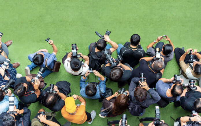 People gathered on a green field, taking photographs in a lively outdoor setting.