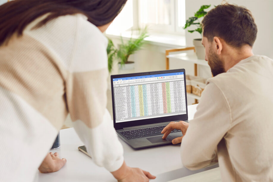 A man and woman review a spreadsheet together on a laptop, discussing data and insights.
