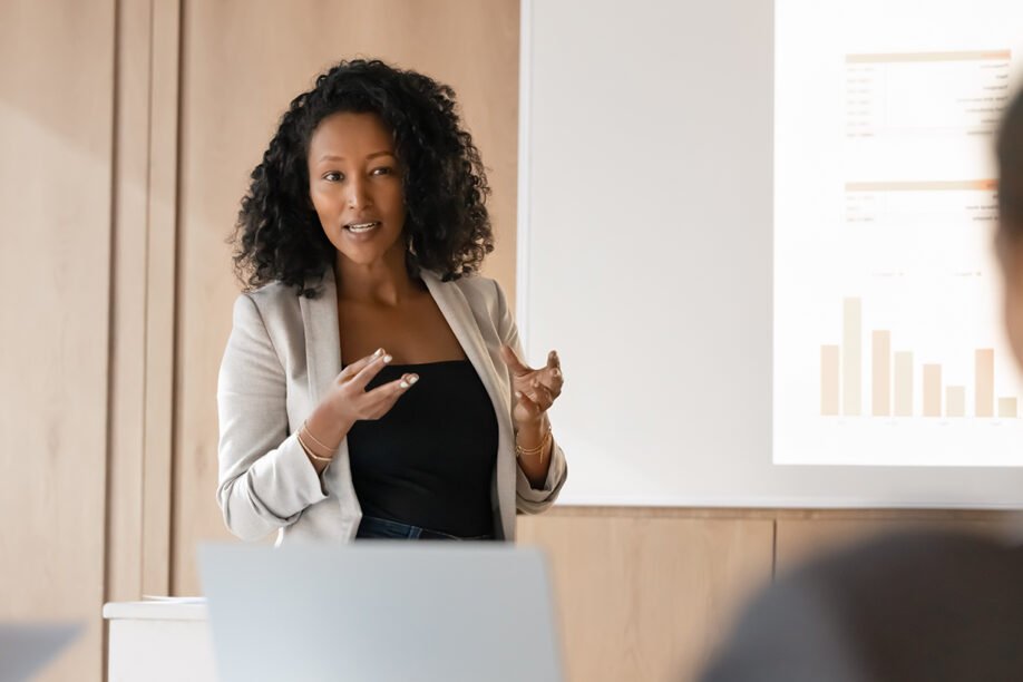 A woman delivers a presentation to a seated audience, using visual aids to enhance her message.